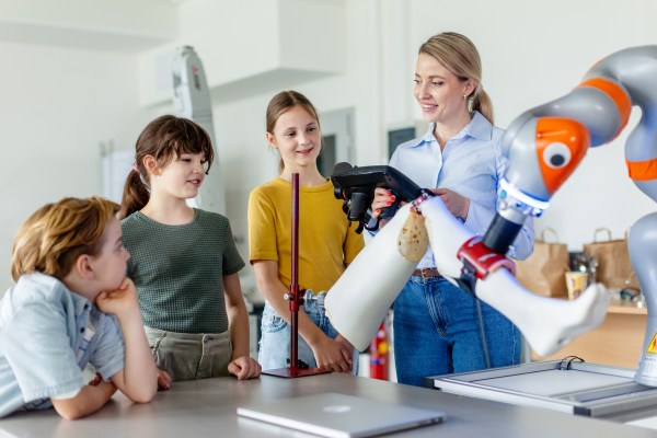 Field trip to real robotics laboratory, encouraging children in career in robotics. Real scientist talking with young students, showing them a robotic arm.