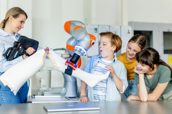 Field trip to real robotics laboratory, encouraging children in career in robotics. Real scientist talking with young students, showing them a robotic arm.