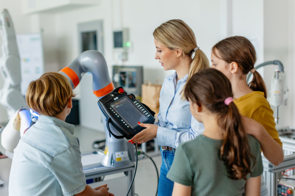 Field trip to real robotics laboratory, encouraging children in career in robotics. Real scientist talking with young students, showing them a robotic arm.