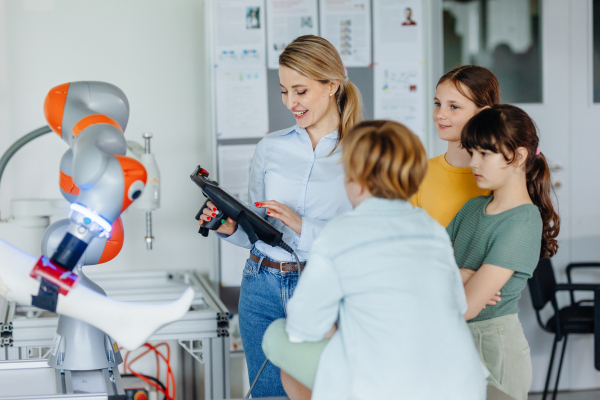 Field trip to real robotics laboratory, encouraging children in career in robotics. Real scientist talking with young students, showing them a robotic arm.