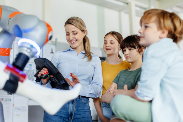 Field trip to real robotics laboratory, encouraging children in career in robotics. Real scientist talking with young students, showing them a robotic arm.