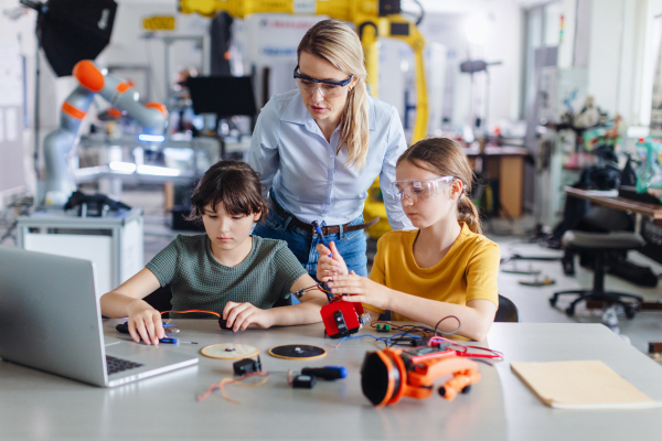 Female teacher helping to girls working on small robot, building robotic car in after-school robotics club. Children learning robotics in Elementary school. Girls in science, STEM.