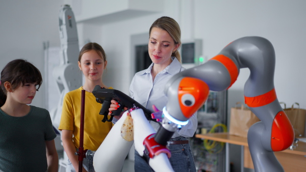 Field trip to real robotics laboratory, encouraging children in career in robotics. Real scientist talking with young students, showing them a robotic arm.