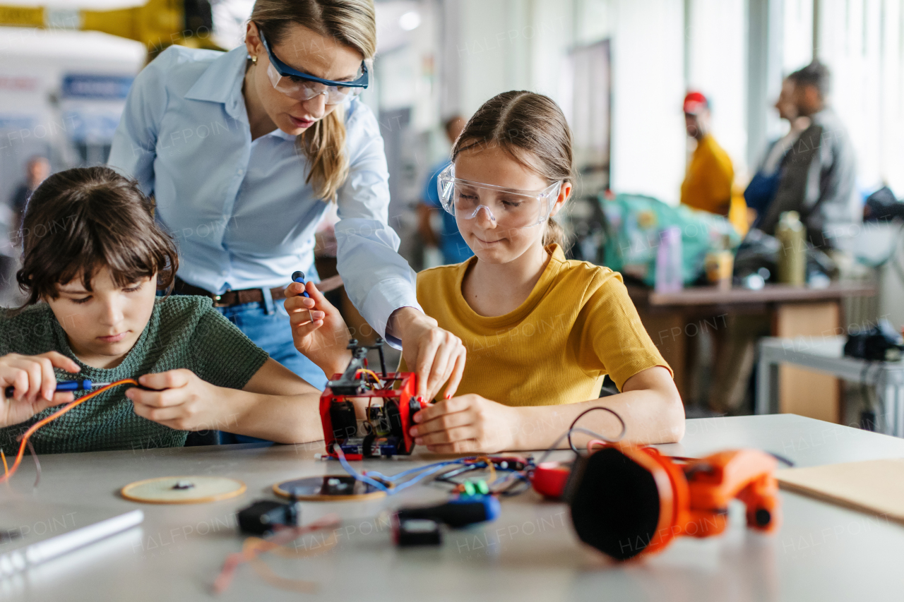 Female teacher helping to girls working on small robot, building robotic car in after-school robotics club. Children learning robotics in Elementary school. Girls in science, STEM.