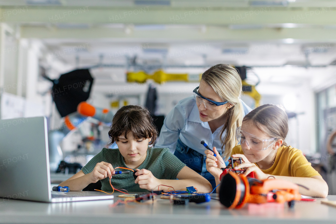 Female teacher helping to girls working on small robot, building robotic car in after-school robotics club. Children learning robotics in Elementary school. Girls in science, STEM.