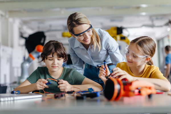 Female teacher helping to girls working on small robot, building robotic kit in after-school robotics club. Children learning robotics in Elementary school. Girls in science, STEM.