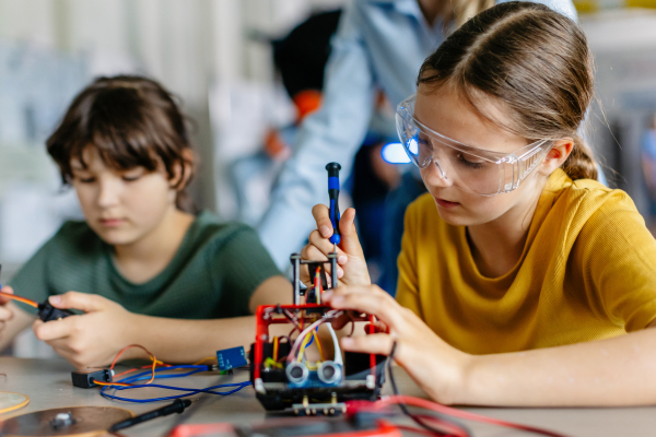 School girls working on circuit board of small robot, building robotic car in after-school robotics club. Children learning robotics in Elementary school. Girls in science, STEM.