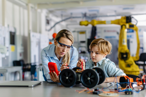 Female teacher helping young schoolboy to build robotic car in after-school robotics club. Children learning robotics in Elementary school. Science for kids. STEM.