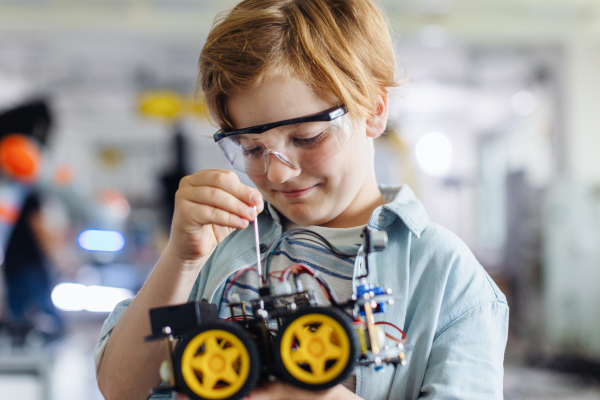 Portrait of focused schoolboy building robotic car in after-school robotics club. Children learning robotics in Elementary school. Science for kids.