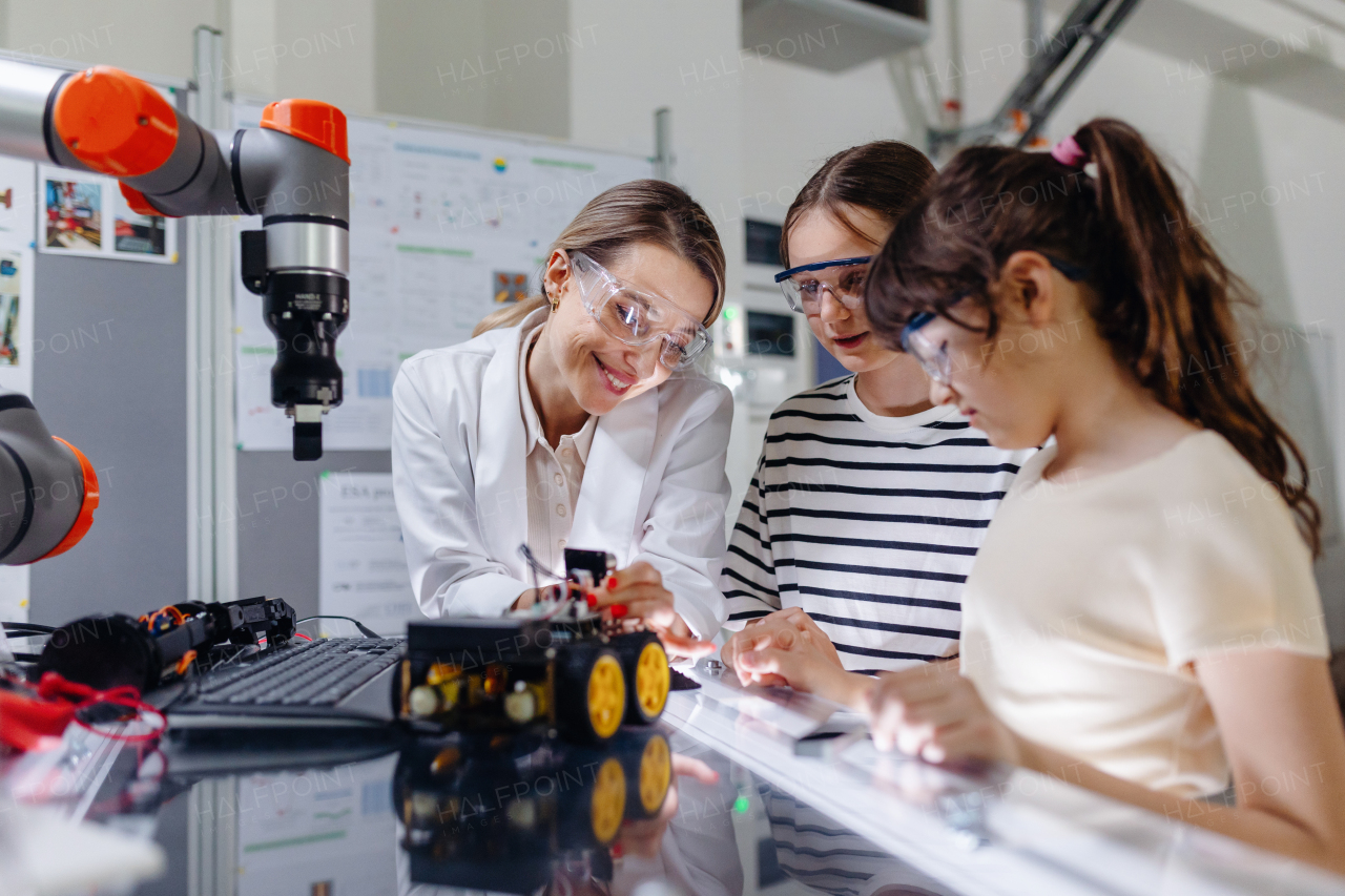 Female teacher helping to girls working on small robot, building robotic car in after-school robotics club. Children learning robotics in Elementary school. Girls in science, STEM.