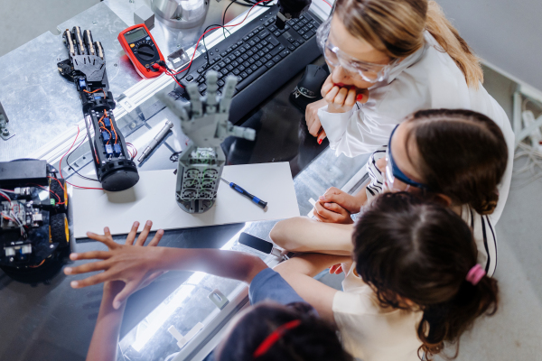 High angle view of teacher helping to girls working on small robot, building robotic kit in after-school robotics club. Children learning robotics in Elementary school. Girls in science, STEM.