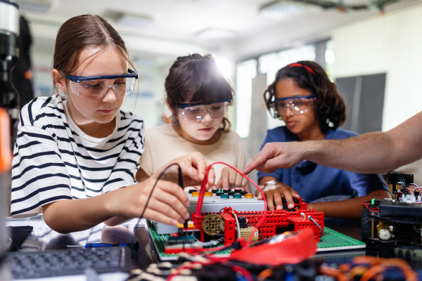 Classmates working togeter on circuit board, building robot in an after-school robotics club. Children learning robotics in Elementary school.