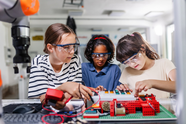 Classmates working togeter on circuit board, building robot in an after-school robotics club. Children learning robotics in Elementary school.