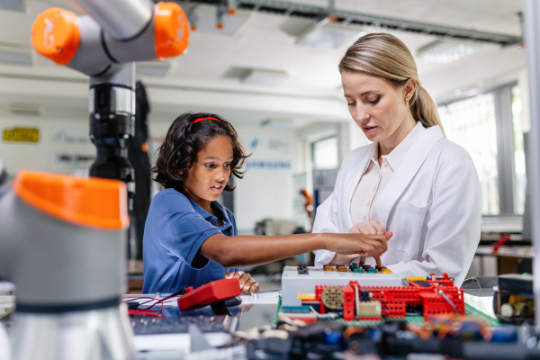 Female teacher helping young schoolboy to build robot kit in after-school robotics club. Children learning robotics in Elementary school. Science for kids. STEM.