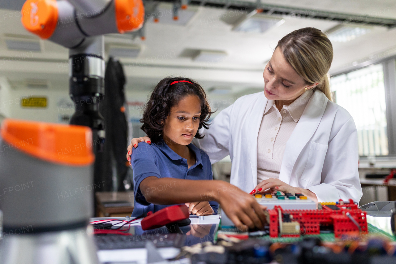 Female teacher helping young schoolboy to build robot kit in after-school robotics club. Children learning robotics in Elementary school. Science for kids. STEM.