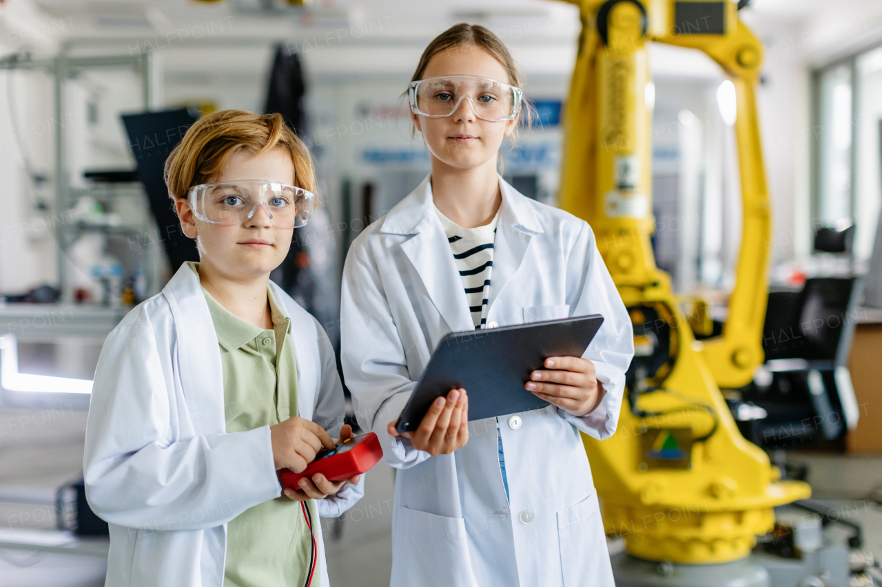 Two classmates standing in a robotic laboratory, wearing lab coats and safety eyeglasses. After-school robotics club. Children learning robotics in Elementary school.