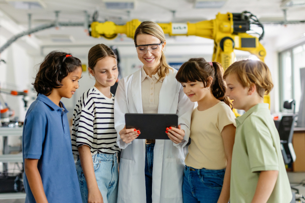 Portrait of children learning robotics in Elementary school, standing with female teacher. Young students building robot in after school robotics club. Field trip to real robotics laboratory.