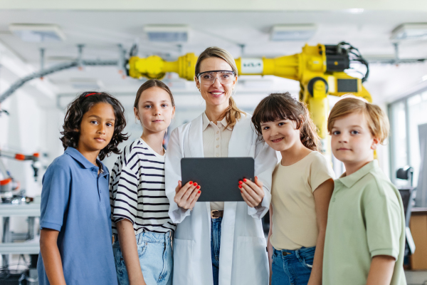 Portrait of children learning robotics in Elementary school, standing with female teacher. Young students building robot in after school robotics club. Field trip to real robotics laboratory.