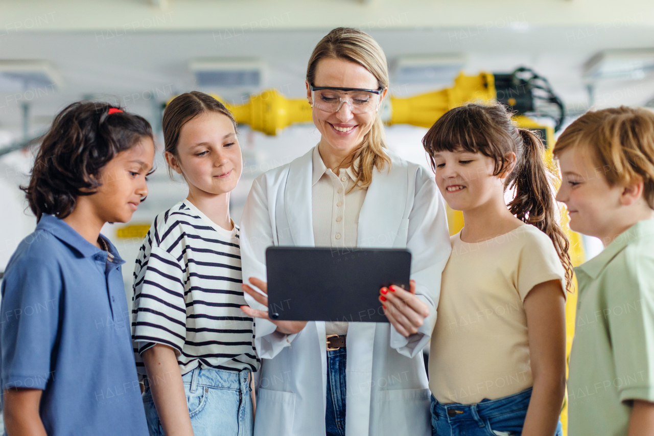 Children learning robotics in Elementary school, standing with female teacher, looking at tablet.Young students building robot in after school robotics club. Field trip to real robotics laboratory.