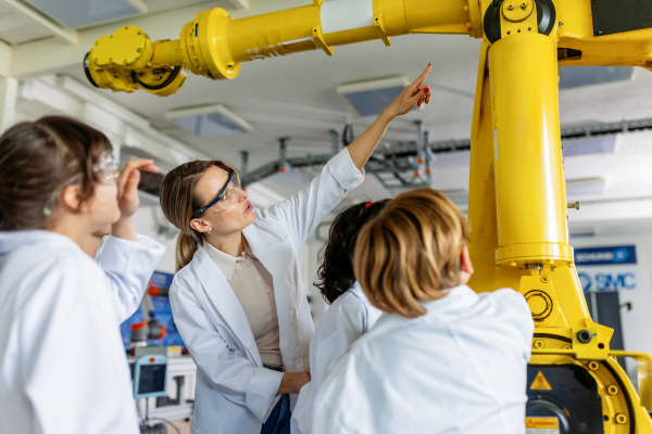 Field trip to real robotics laboratory, encouraging children in career in robotics. Real scientist talking with young students, showing them a robotic arm.