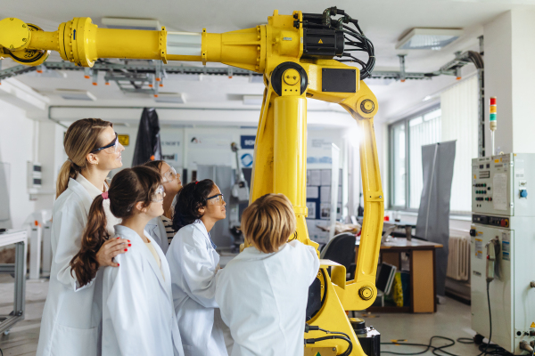 Field trip to real robotics laboratory, encouraging children in career in robotics. Real scientist talking with young students, showing them a robotic arm.