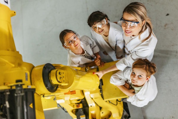 Portrait of children learning robotics in Elementary school, standing with female teacher. Young students building robot in after school robotics club. Field trip to real robotics laboratory.