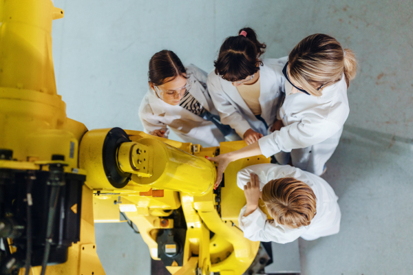 Field trip to real robotics laboratory, encouraging children in career in robotics. Real scientist talking with young students, showing them a robotic arm.