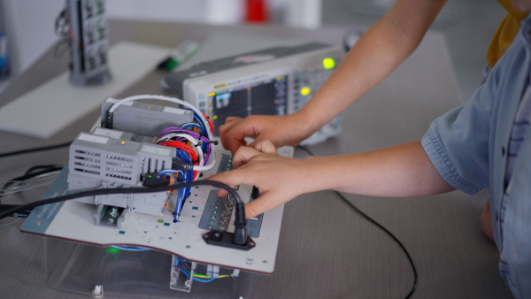 Close up of two classmates working togeter on circuit board, building robot in an after-school robotics club. Children learning robotics in Elementary school.