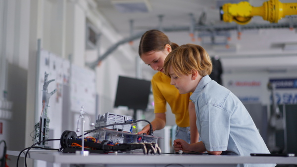 Two classmates working togeter on circuit board, building robot in an after-school robotics club. Children learning robotics in Elementary school.