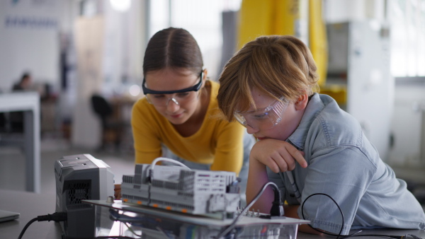 Two classmates working togeter on circuit board, building robot in an after-school robotics club. Children learning robotics in Elementary school.