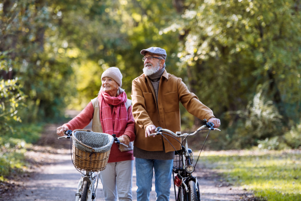 Lovely elderly couple on walk in the forest, pushing their bikes side by side. Seniors in love on stroll through autumn nature, enjoying a peaceful moment together.