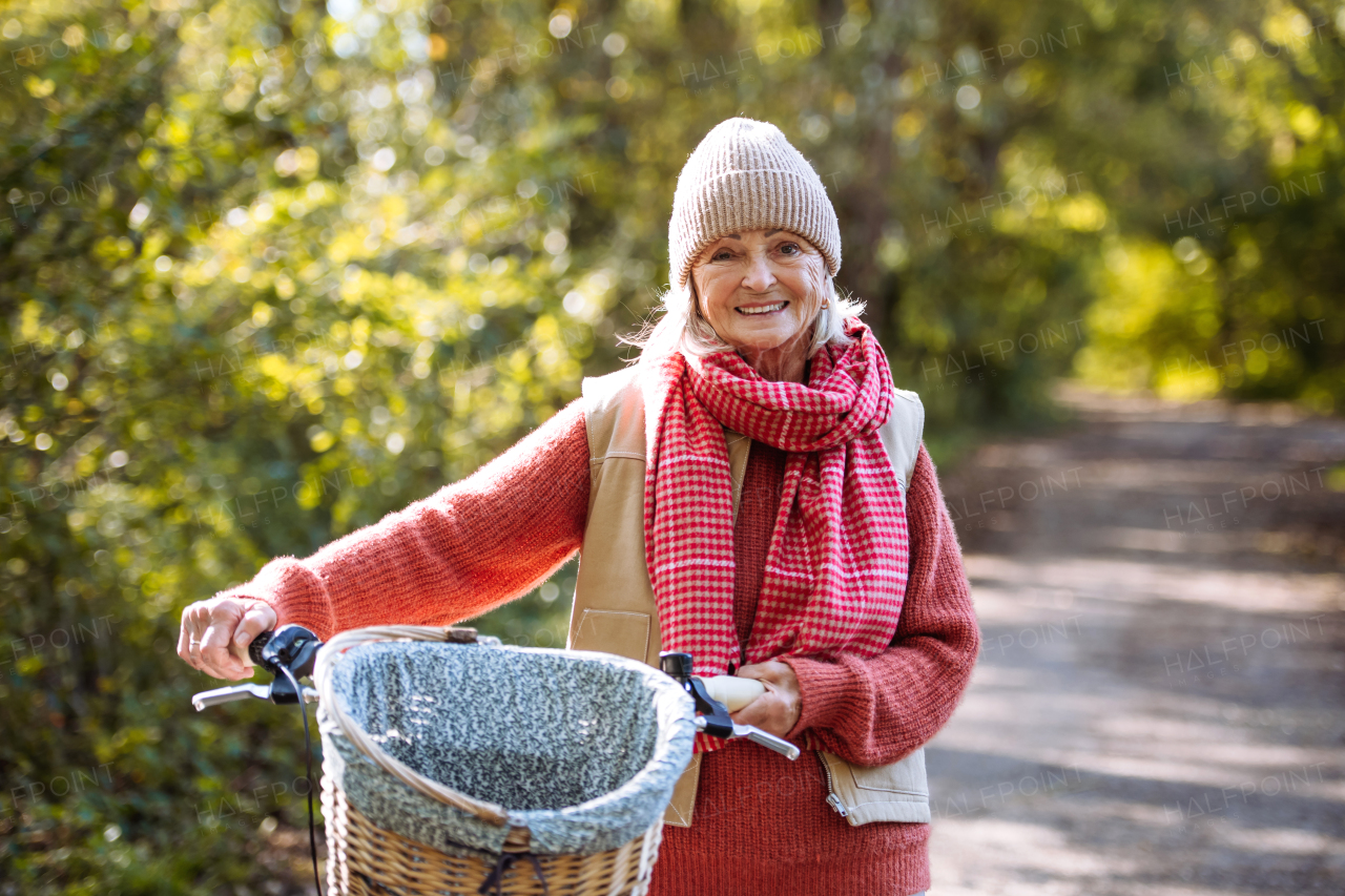 Beautiful elderly woman on a walk in the forest, pushing bike by her sid. Female senior enjoying peaceful moment in autumn nature.