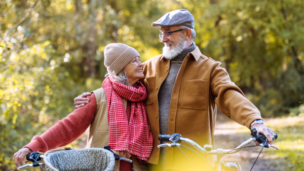 Lovely elderly couple on walk in the forest, pushing their bikes side by side. Seniors in love on stroll through autumn nature, enjoying a peaceful moment together.