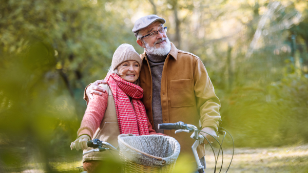 Portrait of elderly couple with bikes in the forest. Seniors in love on stroll through autumn nature, enjoying a peaceful moment together.