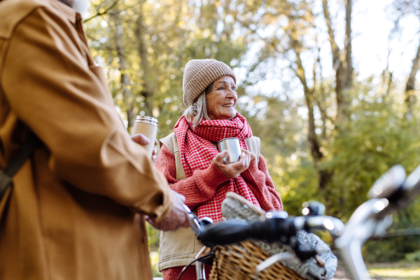 Lovely elderly couple on standing in the middle of autumn nature with their bikes, enjoying cup of hot coffee from thermos.