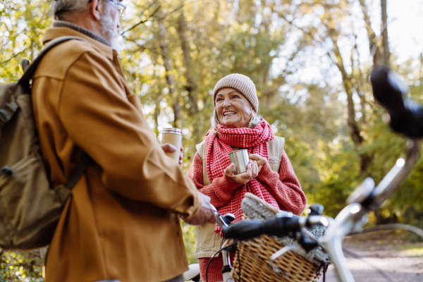 Lovely elderly couple on standing in the middle of autumn nature with their bikes, enjoying cup of hot coffee from thermos.