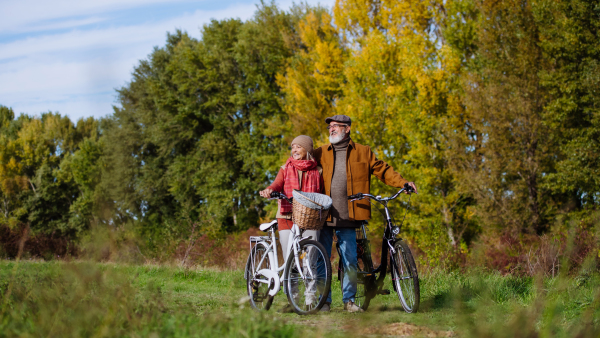 Lovely elderly couple on walk in the forest, pushing their bikes side by side. Seniors in love on stroll through autumn nature, enjoying a peaceful moment together.