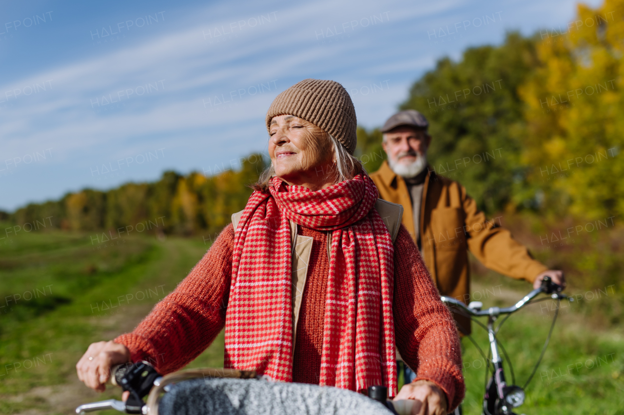 Lovely elderly couple on walk in the forest, pushing their bikes side by side. Seniors in love on stroll through autumn nature, enjoying a peaceful moment together.