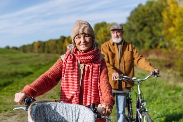 Elderly couple on walk in the forest, pushing their bikes side by side. Seniors in love on stroll through autumn nature, enjoying a peaceful moment together.