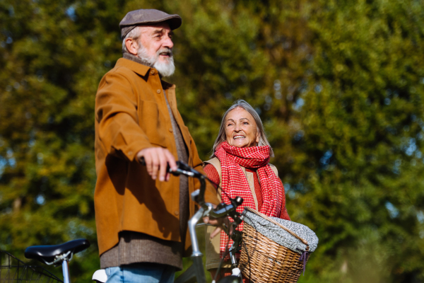 Lovely elderly couple on walk in the forest, pushing their bikes side by side. Seniors in love on stroll through autumn nature, enjoying a peaceful moment together.