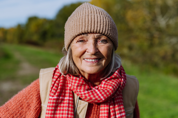 Portrait of beautiful older woman with a gray hair. Female senior standing outdoors in nature, looking at camera, smiling.