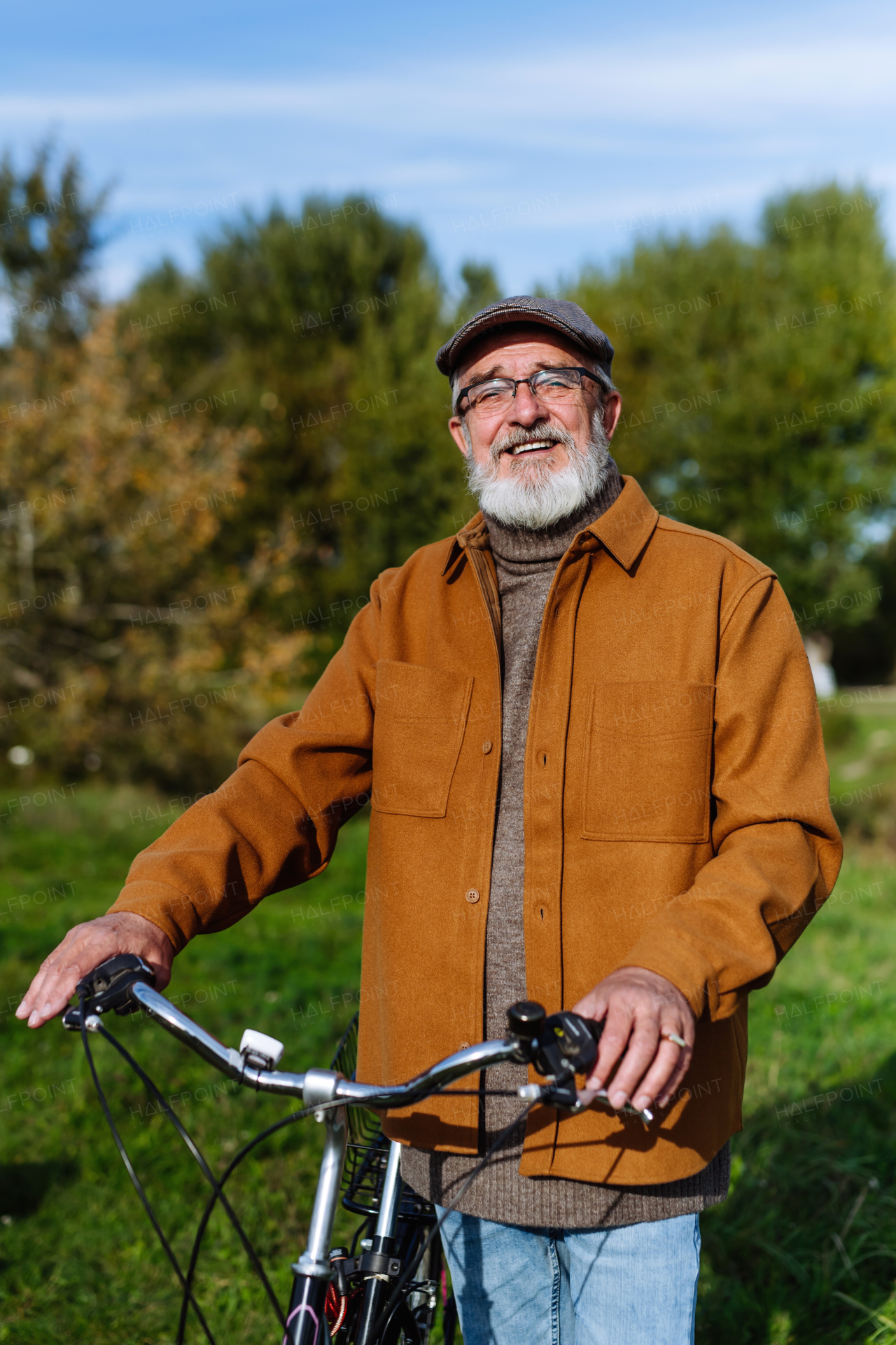 Portrait of friendly older man with gray beard. Senior standing outdoors in nature, looking at camera and smiling.