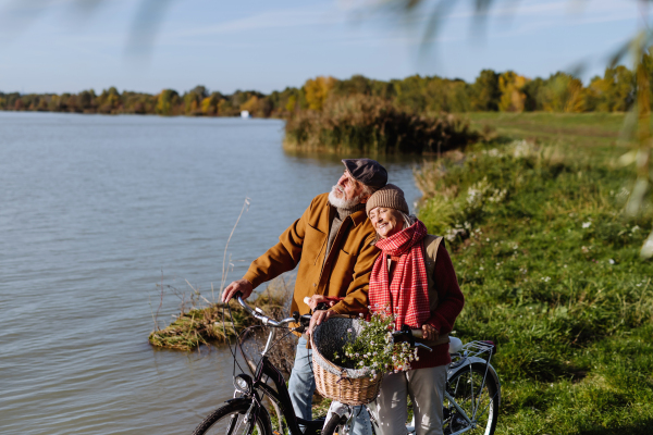 Lovely elderly couple on standing by lake with their bikes, enjoying peaceful moment together.