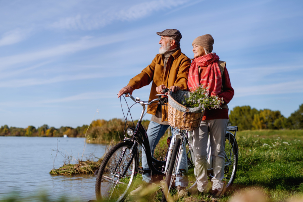 Lovely elderly couple on standing by lake with their bikes, enjoying peaceful moment together.