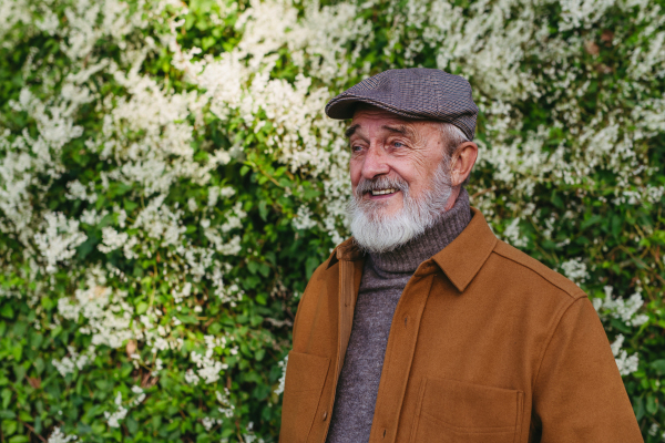 Portrait of friendly older man with gray beard. Senior standing outdoors in nature, smiling.