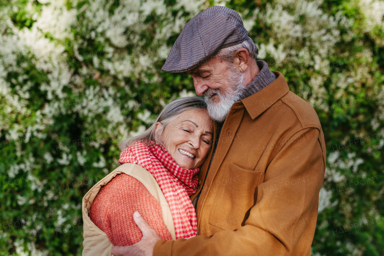 Portrait of beautiful senior couple outdoors in autumn garden. Elderly husband and wife are embracing each other.