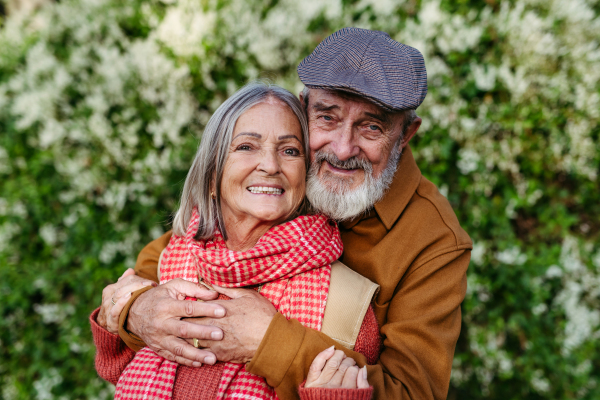 Portrait of beautiful senior couple outdoors in autumn garden. Elderly husband and wife are embracing each other.