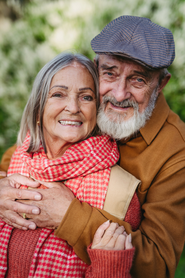 Portrait of beautiful senior couple outdoors in autumn garden. Elderly husband and wife are embracing each other.