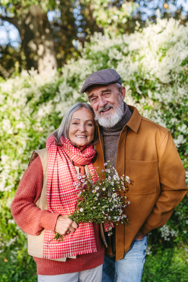 Portrait of beautiful senior couple outdoors in autumn garden. Elderly husband and wife are embracing each other.