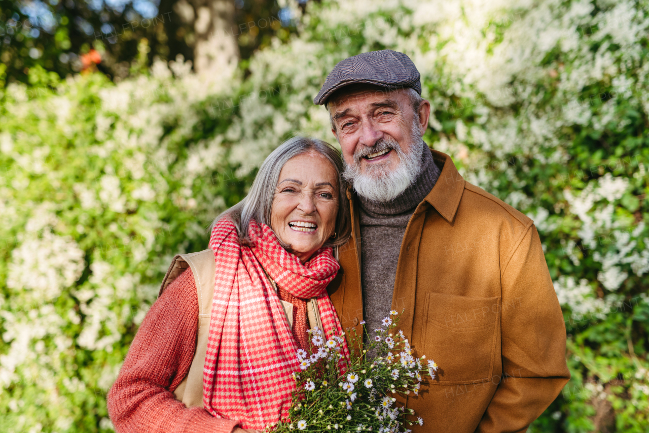 Portrait of beautiful senior couple outdoors in autumn garden. Elderly husband and wife are embracing each other.